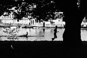 Silhouette of a runner and a rower moving along the same riverside path at dusk