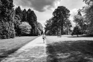 Woman walking along a straight path, sunlit on one side and shaded on the other, framed by trees