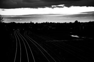 Railway tracks converging toward the horizon at dusk, trees silhouetted alongside.